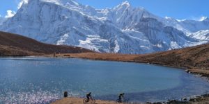 Mountain bikers riding on the shores of Kicho Tal (Ice Lake) above Manang on the Annapurna Circuit in Nepal. The who of the Annapurna Massive is in the background.